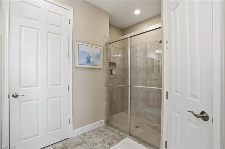 Full shower enclosure featuring a tiled interior, glass sliding doors, and integrated lighting