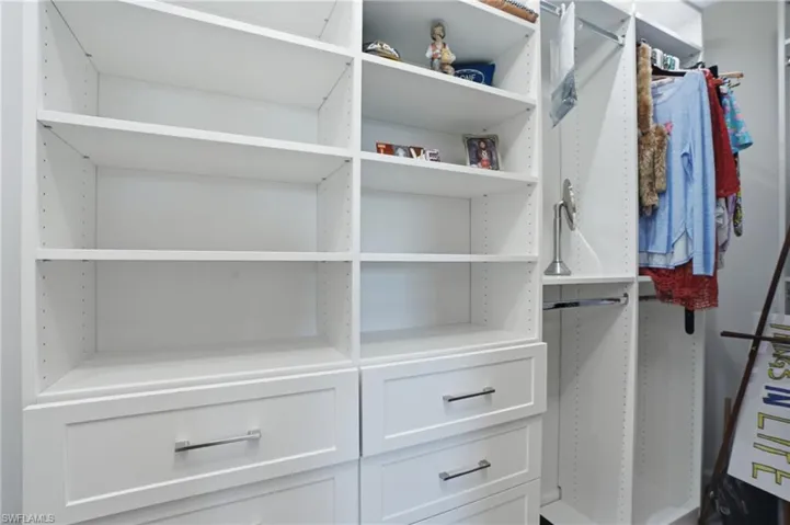 Custom closet system featuring white built-in shelving, multiple hanging rods, and pull-out drawers with chrome hardware