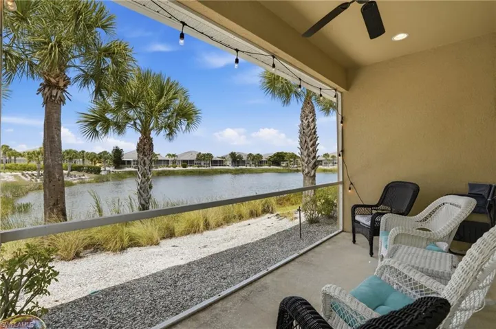 Screened porch with concrete flooring and a ceiling fan, overlooking a body of water with established palm trees and natural landscaping