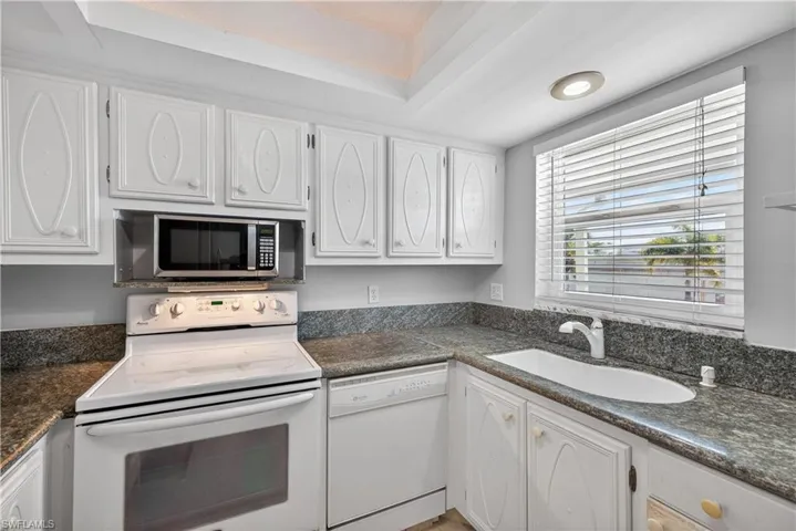 Kitchen featuring white cabinets, granite counters, and a tray ceiling with cove lighting.