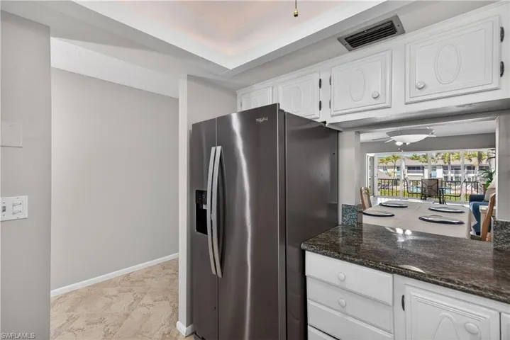 Kitchen featuring stainless steel fridge with ice dispenser, white cabinets, granite counters, and a pass through window to the dining room with views of the courtyard and pool.