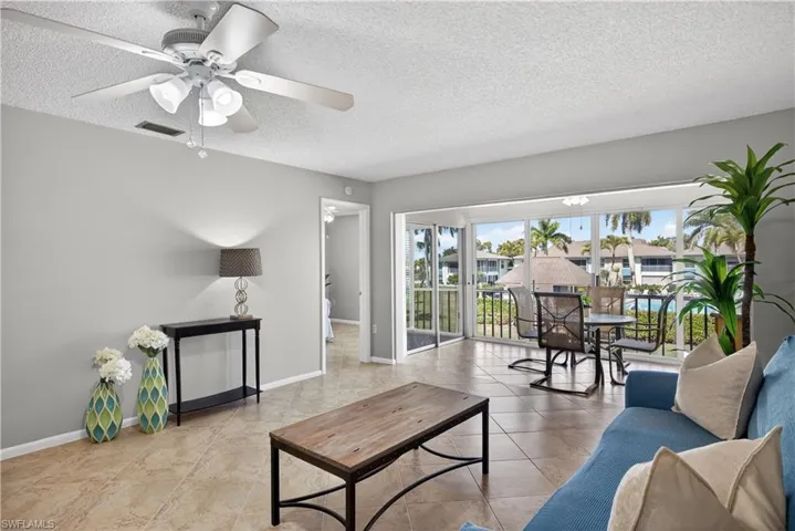 Living room featuring a ceiling fan/light, tile floors and views of the courtyard and pool