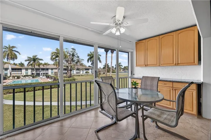 Sunroom with sliding doors, a ceiling fan/light, bar area with cabinets and granite counters overlooking the courtyard and pool.