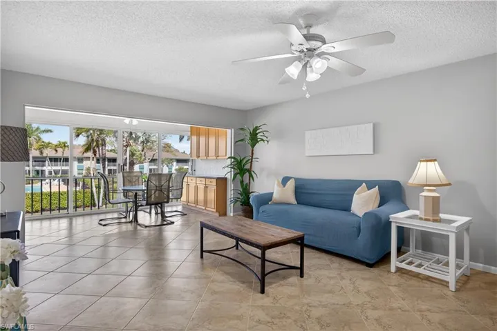 Living room featuring a ceiling fan/light, tile floors and views of the courtyard and pool