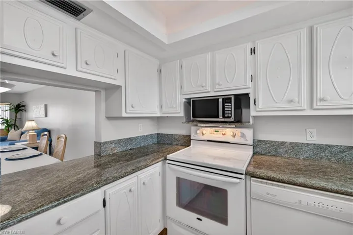 Kitchen featuring white cabinets, granite counters, and a tray ceiling with cove lighting.