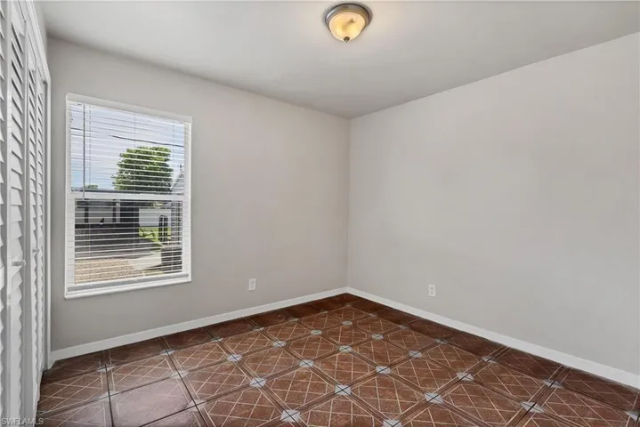 Patterned floor tiling, neutral wall tones, window with horizontal blinds, and a flush-mount ceiling light