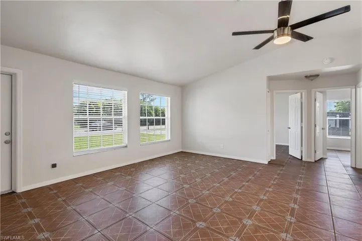 Vaulted ceiling, modern ceiling fan, patterned tile flooring, dual windows with blinds, and white interior doors