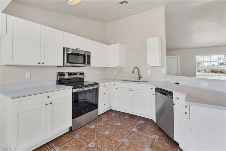 Kitchen with white cabinetry, stainless steel appliances, light-toned countertops, and decorative floor tiling