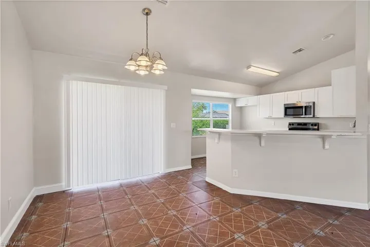 Vaulted ceiling with an attached chandelier, ceramic tile flooring, sliding glass door, white cabinetry, and stainless steel microwave