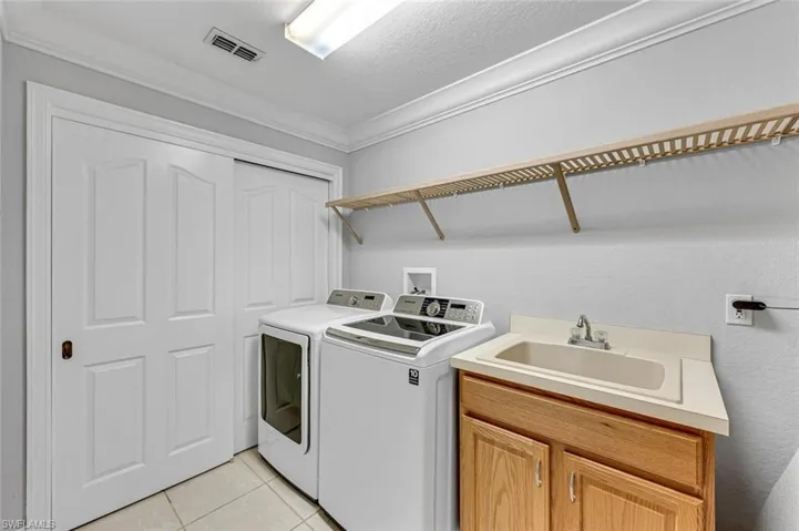 Laundry room featuring washing machine and dryer, a sink, light tile patterned floors, visible vents, and cabinet space