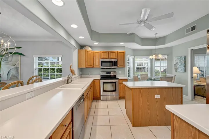 Kitchen with a wealth of natural light, a sink, appliances with stainless steel finishes, ceiling fan with notable chandelier, and visible vents