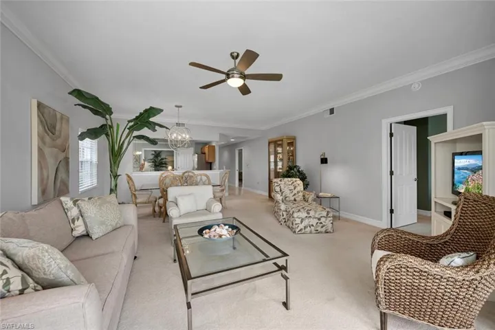 Living area with light colored carpet, ornamental molding, ceiling fan with notable chandelier, baseboards, and visible vents