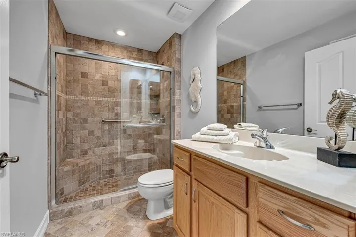 Bathroom featuring visible vents, stone finish floor, a shower stall, toilet, and vanity