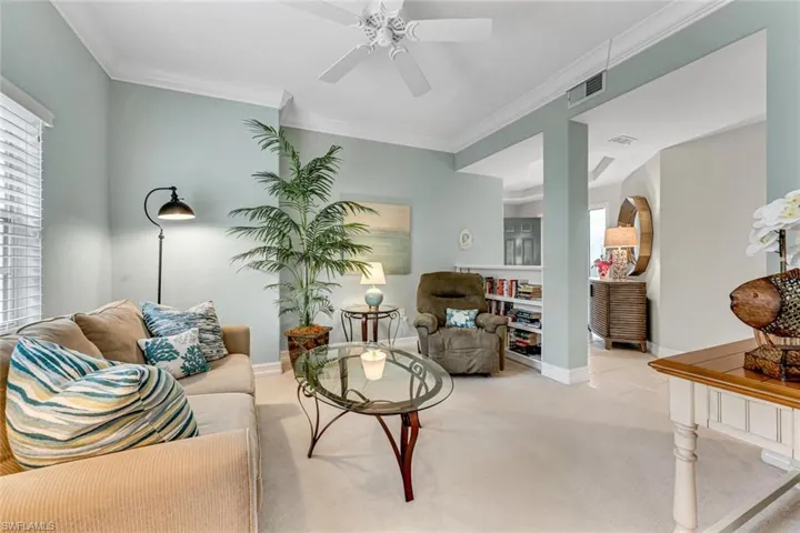 Living area with visible vents, baseboards, ornamental molding, ceiling fan, and light colored carpet