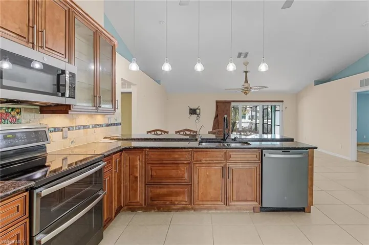 Kitchen featuring lofted ceiling, sink, dark stone countertops, light tile patterned floors, and stainless steel appliances