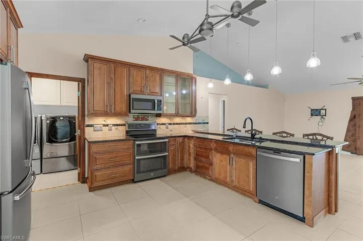 Kitchen featuring sink, dark stone countertops, appliances with stainless steel finishes, ceiling fan, and washer and clothes dryer
