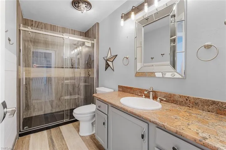 Bathroom with hardwood / wood-style flooring, vanity, a shower with shower door, and toilet