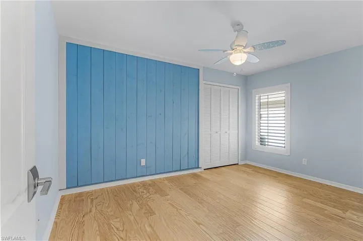 Unfurnished bedroom with light hardwood / wood-style flooring, wooden walls, and ceiling fan