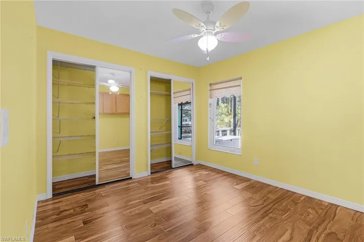 Unfurnished bedroom with ceiling fan, wood-type flooring, and multiple closets