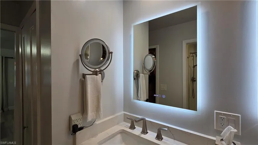 Bathroom vanity featuring a lighted mirror, dual-handle faucet, and white countertop