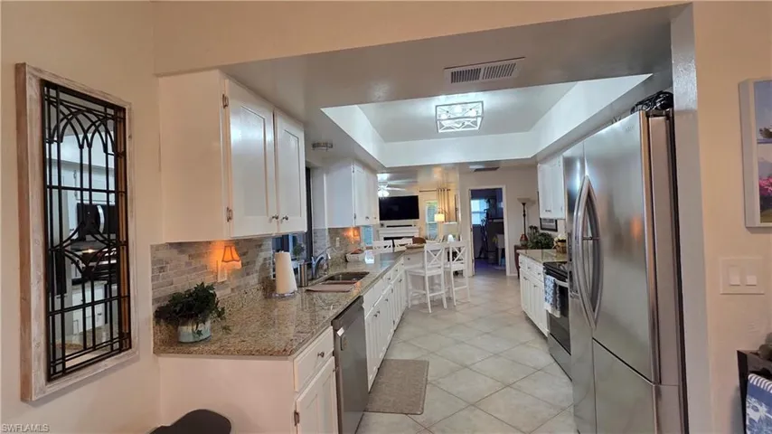Contemporary kitchen featuring white cabinetry, stainless steel appliances, granite countertops, and a subway tile backsplash