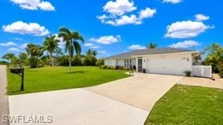 Single-story residence featuring a two-car garage, concrete driveway, and a manicured lawn with mature palm trees