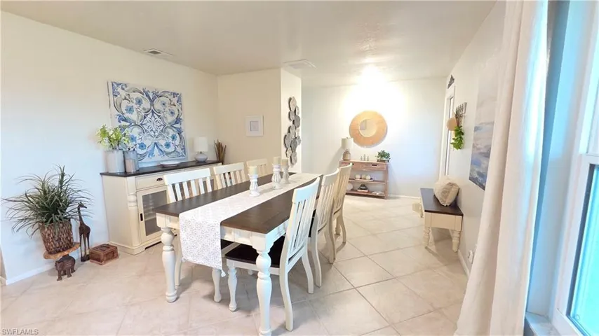 Spacious dining area featuring tile flooring, a dark wood-finish dining table with white chairs, and an elegant side buffet with a dark countertop