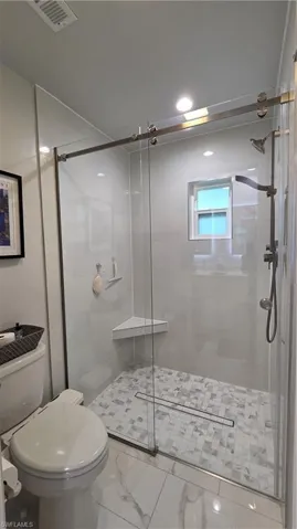 Glass-enclosed shower with a linear drain, mosaic tile flooring, and a corner shelf