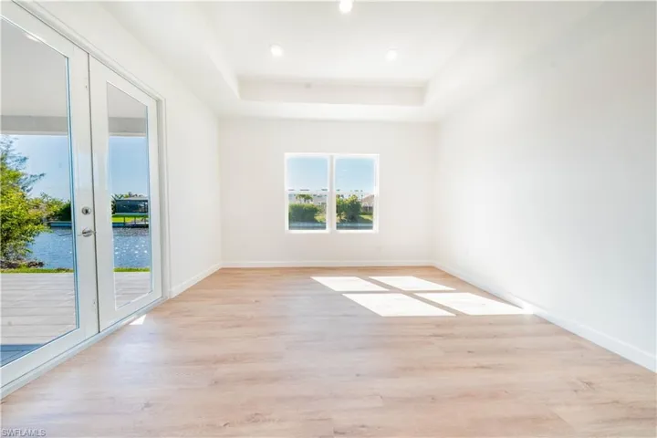 Empty room with light wood-style floors, a water view, a tray ceiling, and recessed lighting