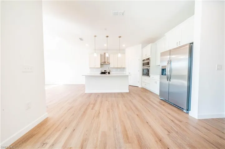 Kitchen featuring stainless steel appliances, white cabinetry, light countertops, pendant lighting, and light wood-style floors