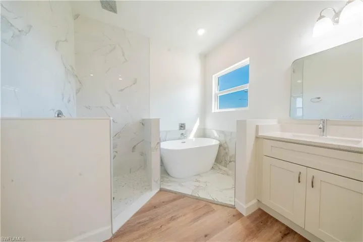 Full bathroom featuring a freestanding tub, a marble finish shower, vanity, light wood-type flooring, and recessed lighting