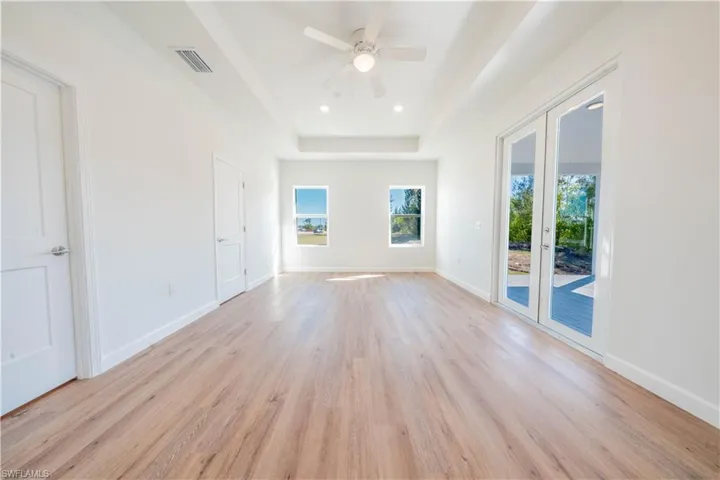Unfurnished room featuring a tray ceiling, light wood finished floors, ceiling fan, french doors, and recessed lighting