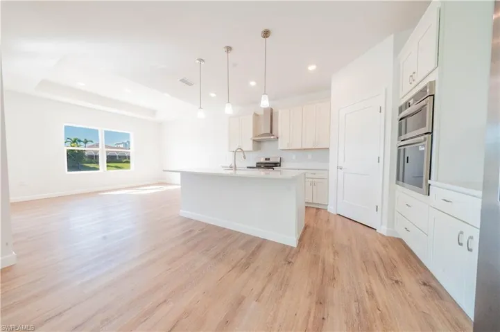 Kitchen featuring open floor plan, an island with sink, hanging light fixtures, white cabinetry, and light wood-type flooring