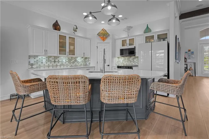 Kitchen with glass insert cabinets, crown molding, white cabinetry, light stone counters, and freestanding refrigerator