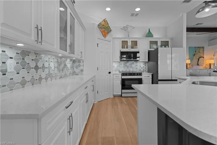 Kitchen featuring white cabinetry, glass insert cabinets, light stone counters, freestanding refrigerator, and electric stove