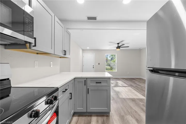 Kitchen featuring kitchen peninsula, appliances with stainless steel finishes, light wood-type flooring, light stone countertops, and gray cabinets
