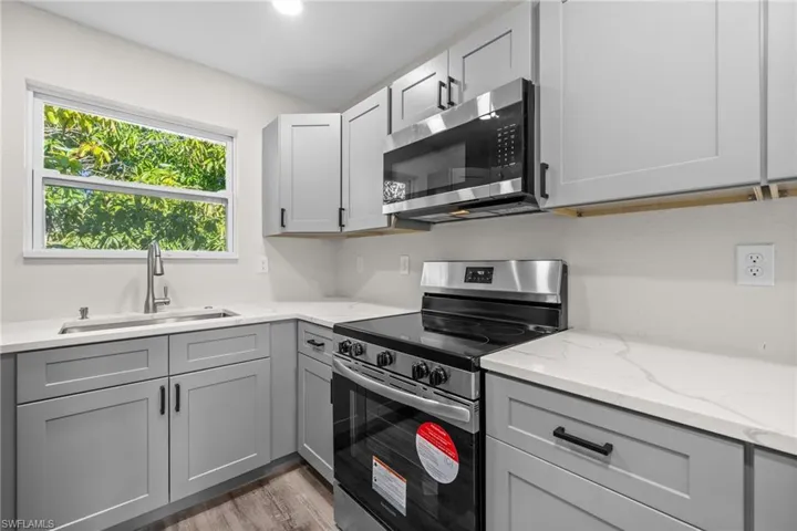 Kitchen featuring light stone countertops, sink, dark hardwood / wood-style floors, gray cabinets, and appliances with stainless steel finishes