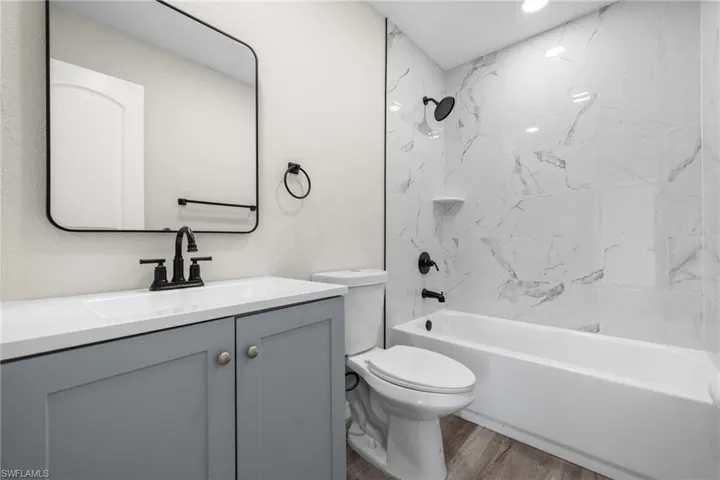 Full bathroom with tiled shower / bath combo, toilet, wood-type flooring, and vanity
