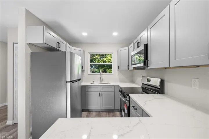 Kitchen with sink, light stone counters, dark hardwood / wood-style flooring, gray cabinets, and appliances with stainless steel finishes