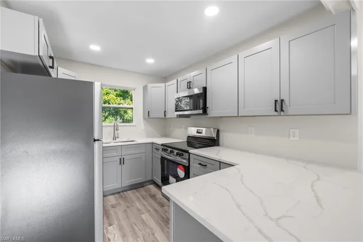 Kitchen with light stone countertops, appliances with stainless steel finishes, sink, light hardwood / wood-style flooring, and gray cabinets