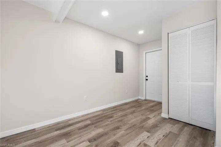 Unfurnished bedroom with beam ceiling, electric panel, a closet, and light hardwood / wood-style floors