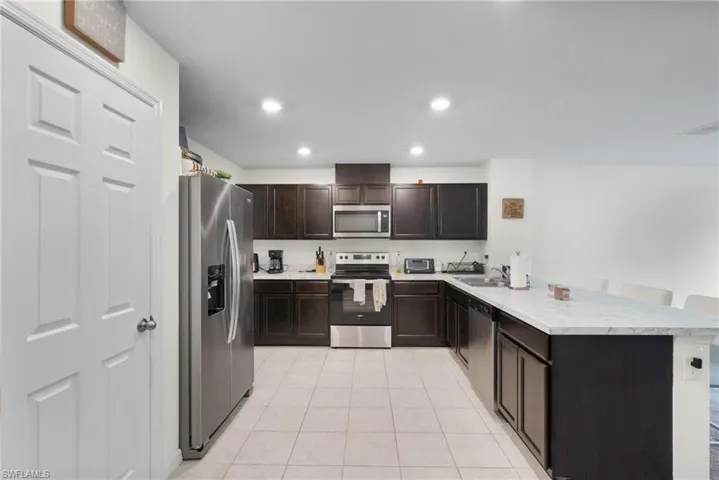 Kitchen with a peninsula, appliances with stainless steel finishes, light tile patterned floors, light countertops, and dark brown cabinetry