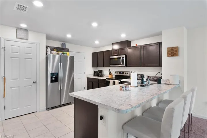 Kitchen featuring appliances with stainless steel finishes, light countertops, a peninsula, dark brown cabinets, and a kitchen bar