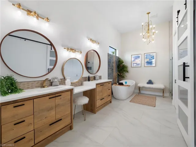 Bathroom with double vanity, a freestanding bath, light marble finish floors, and hanging lights