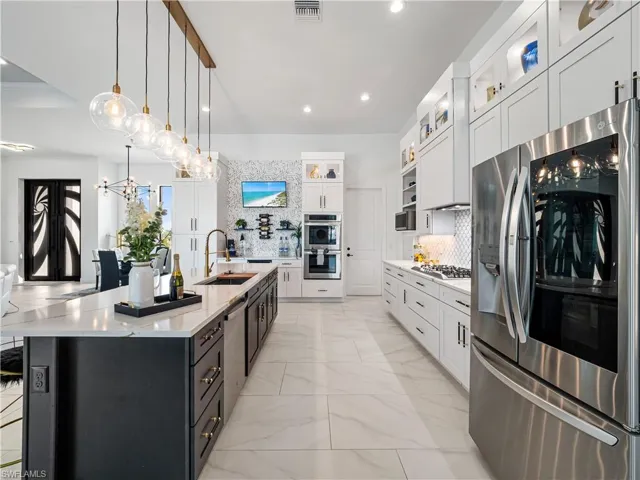 Kitchen with stainless steel appliances, two tone cabinetry, light stone counters, pendant lighting, and backsplash