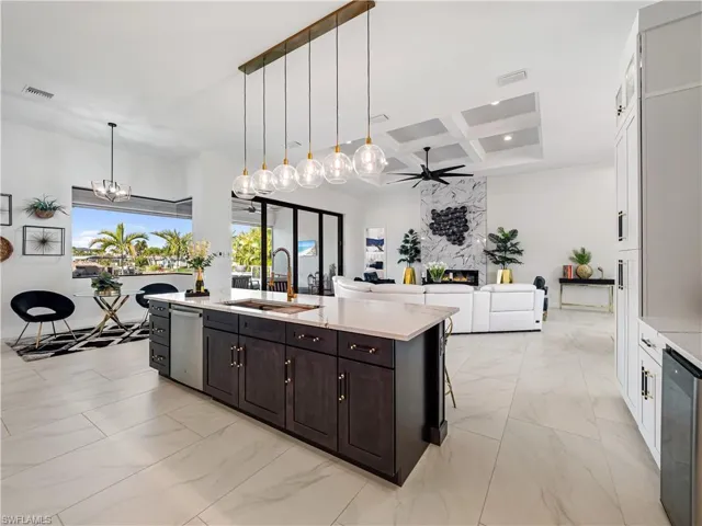 Kitchen with coffered ceiling, open floor plan, light marble finish floors, a center island with sink, and light stone counters