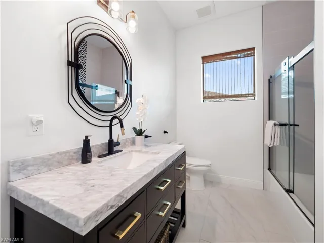 Full bath featuring vanity, bath / shower combo with glass door, and light marble finish floors