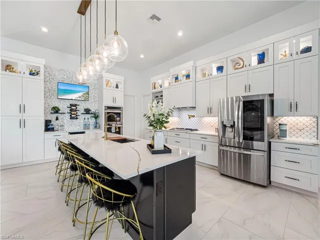 Dual tone kitchen with glass insert cabinets, light marble finish flooring, a breakfast bar area, light stone countertops, and stainless steel appliances