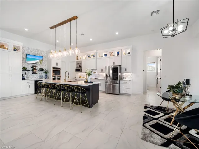 Two tone kitchen featuring glass fronted cabinets, stainless steel appliances, a kitchen breakfast bar, backsplash, and two tone color scheme