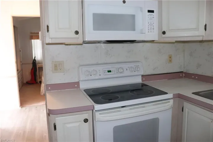 Kitchen with white cabinetry, light countertops, wallpapered walls, and white appliances